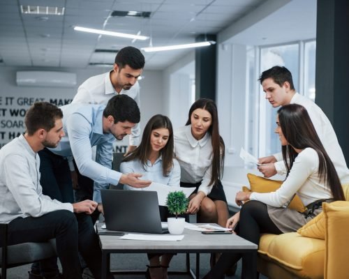 Guy shows document to a girl. Group of young freelancers in the office have conversation and working.
